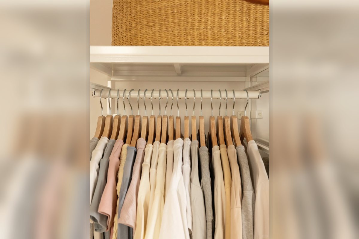 Closet hanging zone with light-colored clothes and upper shelf storage.