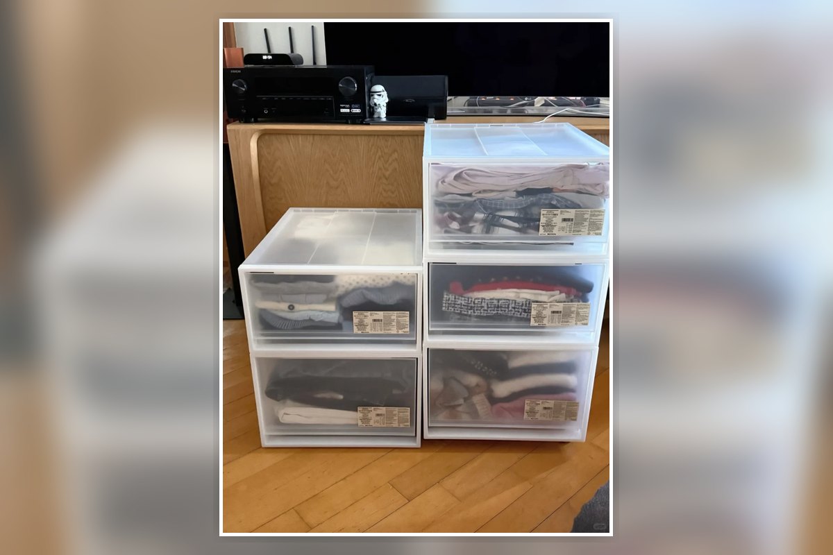 Stacked clear drawer bins holding folded clothes in a small-apartment storage area.