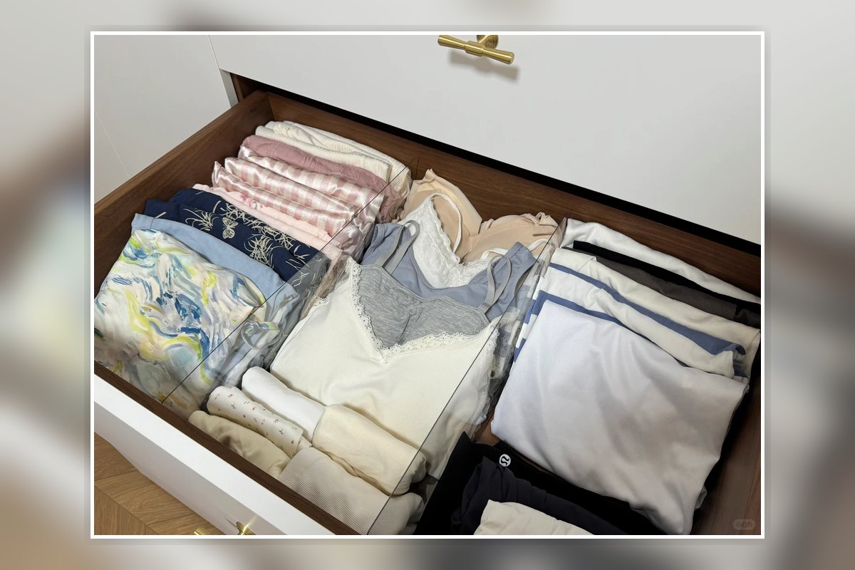 Folded clothes separated into neat sections inside a wide dresser drawer.