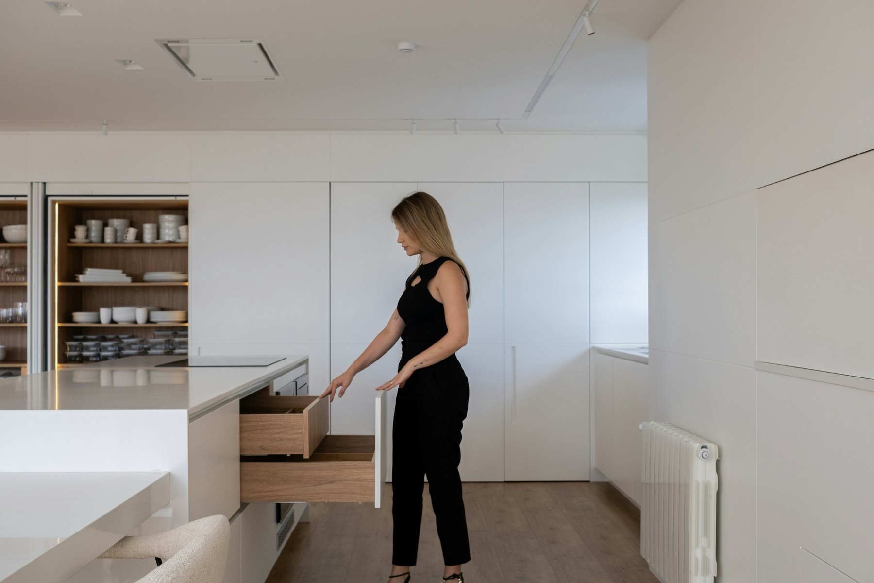 Woman opening a wide wooden pull-out kitchen cabinet drawer in a real white kitchen.