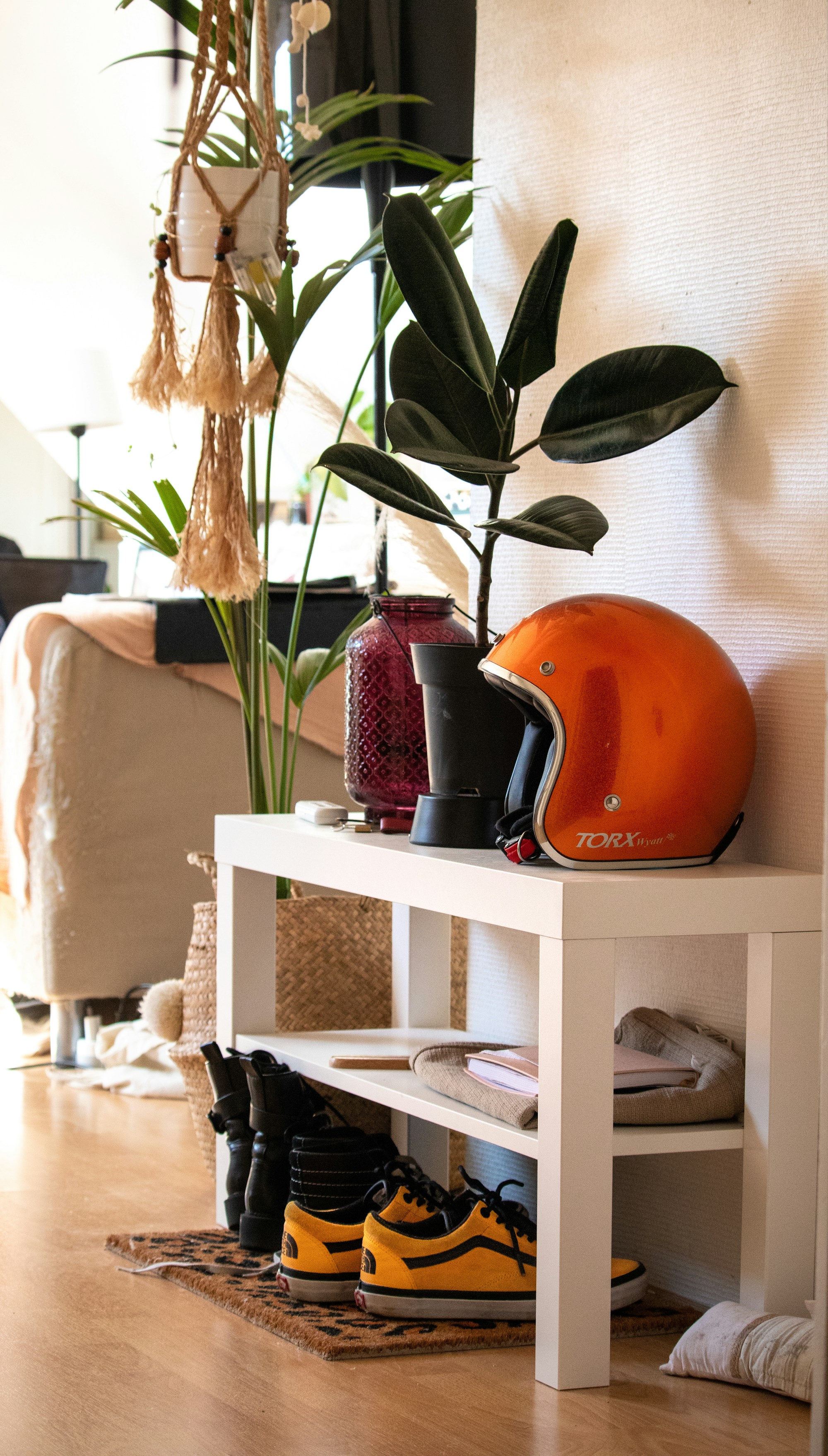 Real apartment entryway with a low white shoe rack holding daily sneakers and boots beneath a narrow console.